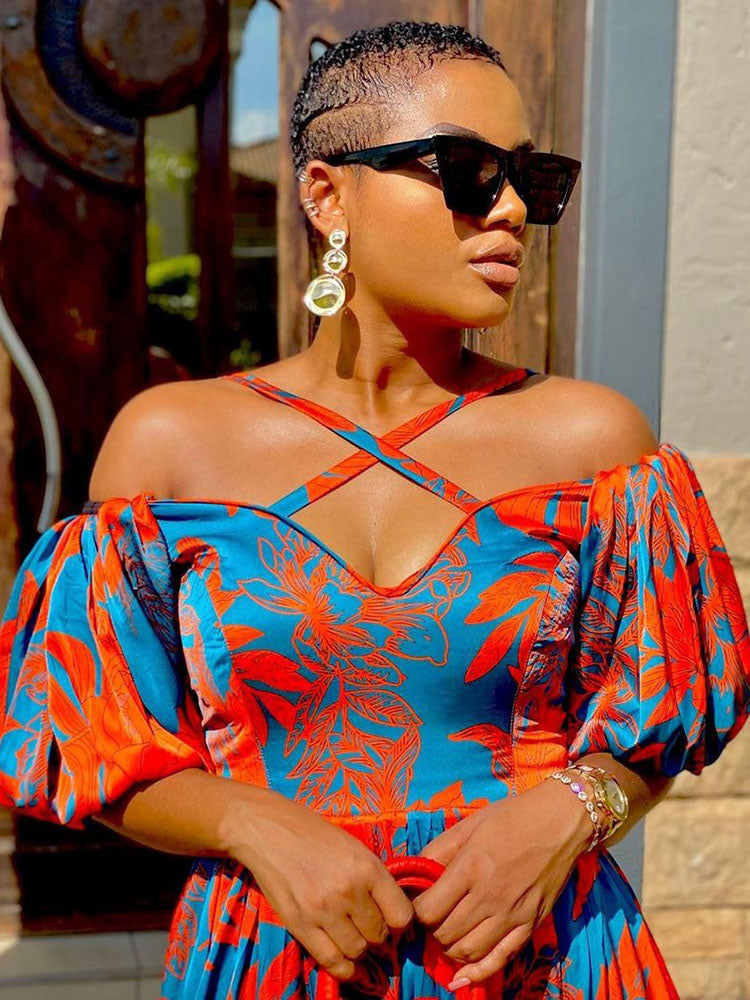 Close-up of a woman's shoulders and chest showcasing the criss-cross neckline and puff sleeves of an orange and blue floral print dress.