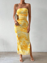 A woman wears a yellow tie-dye print strapless maxi dress with a small white shoulder bag.