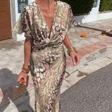 Full-length view of a woman in a green and pink animal print satin maxi dress, accessorized with gold bracelets and a clutch.