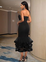 Rear view of a woman wearing a black strapless mermaid dress with a tiered ruffled skirt and ribbon accents.