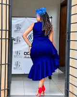 Back view of a woman wearing a royal blue sleeveless dress with ruffle detailing and an asymmetrical hemline.