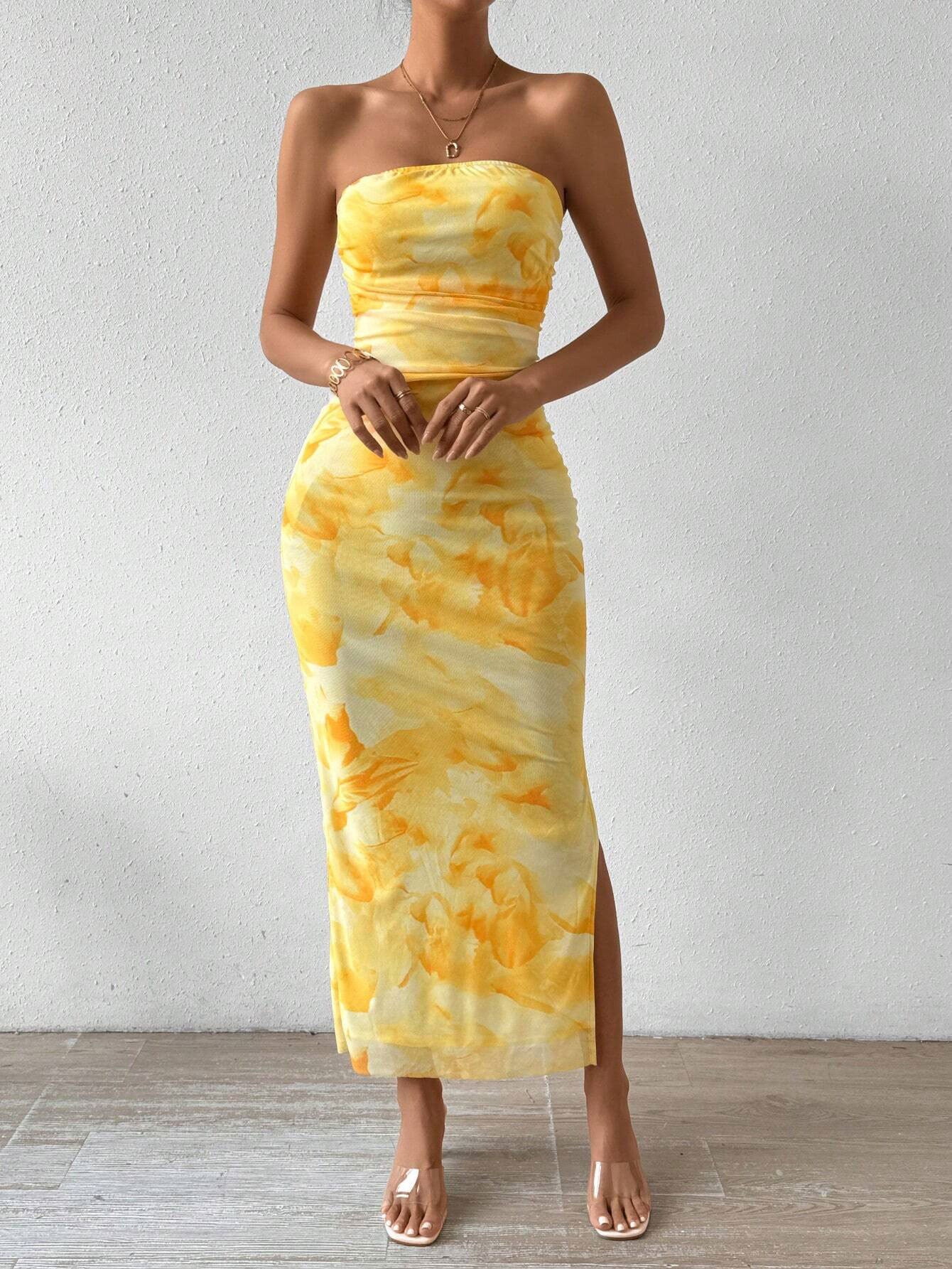 A woman models a yellow tie-dye print strapless maxi dress with a side slit.