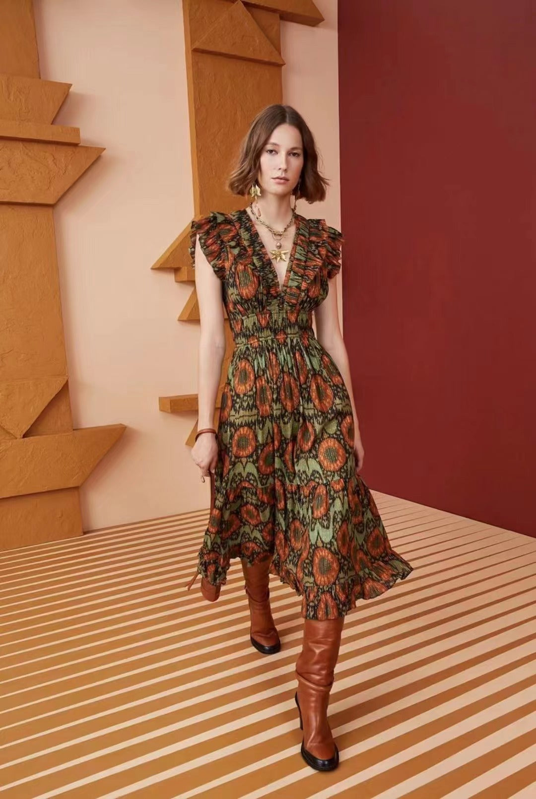 Model posing in a green and orange patterned metallic jacquard midi dress with gold jewelry.