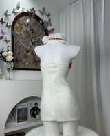 Back view of a white strapless dress with red plaid trim and red ribbon accents, displayed on a mannequin.