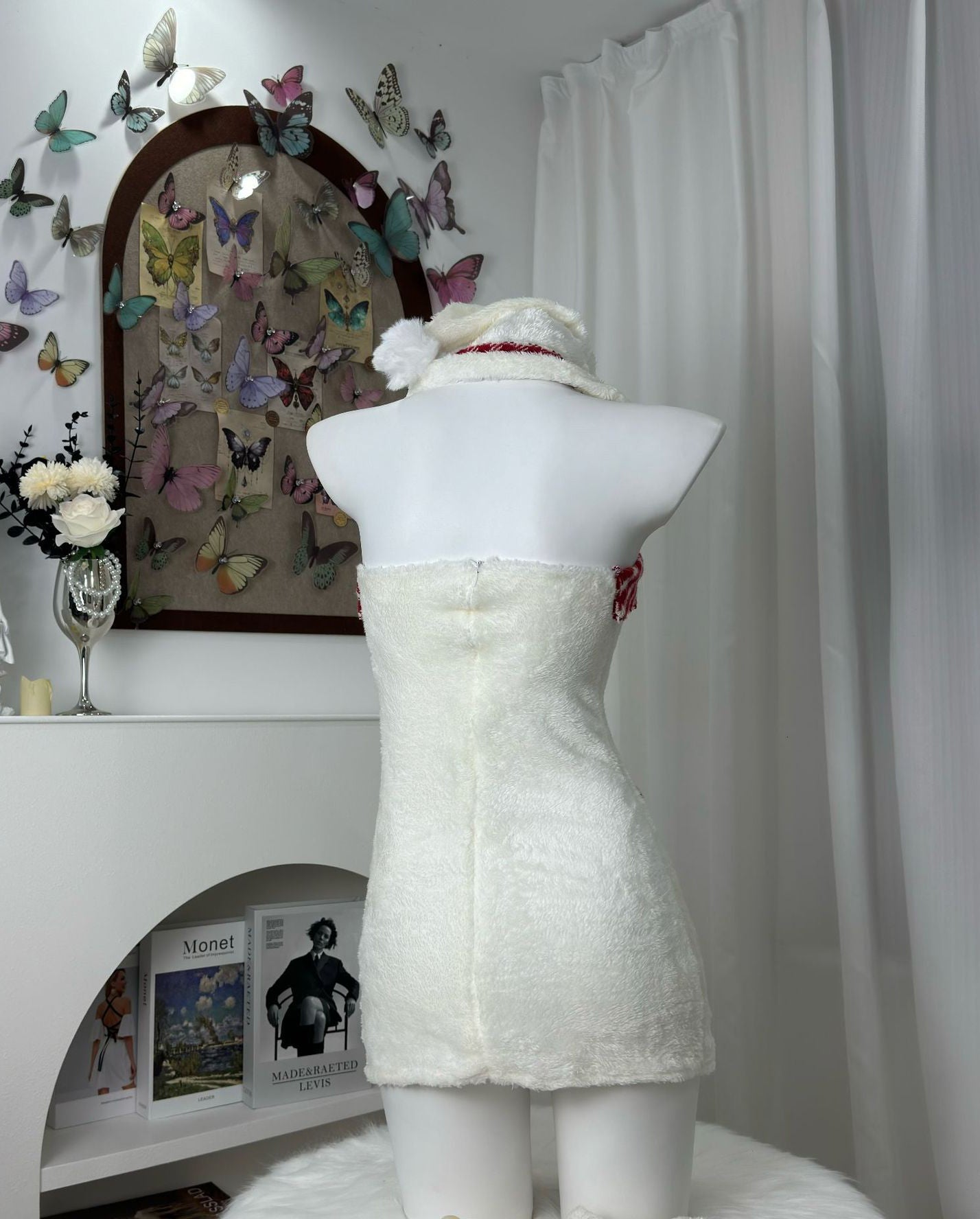 Back view of a white strapless dress with red plaid trim and red ribbon accents, displayed on a mannequin.