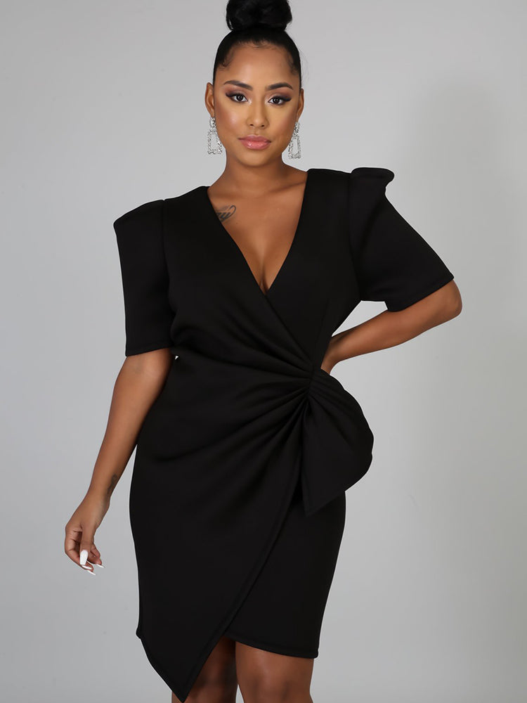 Close-up of a woman in a black V-neck dress with draped knot detail.