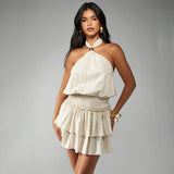 Close-up of a woman wearing a cream halter neck mini dress with a smocked waist and tiered skirt, hands on hips.