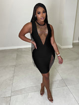 Woman in a black sleeveless dress with embellished neckline and slit, posing with hand on hip