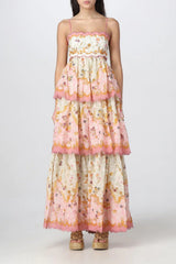 Full-length view of a woman in a tiered floral print maxi dress with cut-out sides and pink pom-pom trim