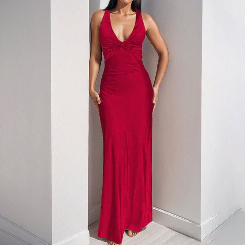 Woman wearing a red satin maxi dress with a twisted V-neckline and halter straps, standing in a corner.