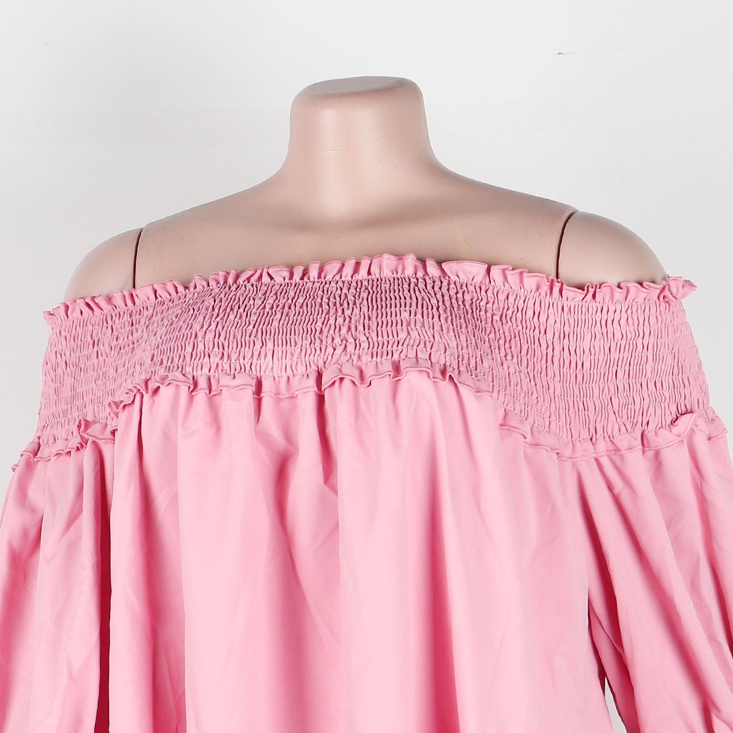 Close-up of the smocked bust and ruffle detail on a pink off-the-shoulder dress.