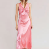 Woman wearing a pink satin maxi dress with a twisted V-neckline and halter straps, against a white background.