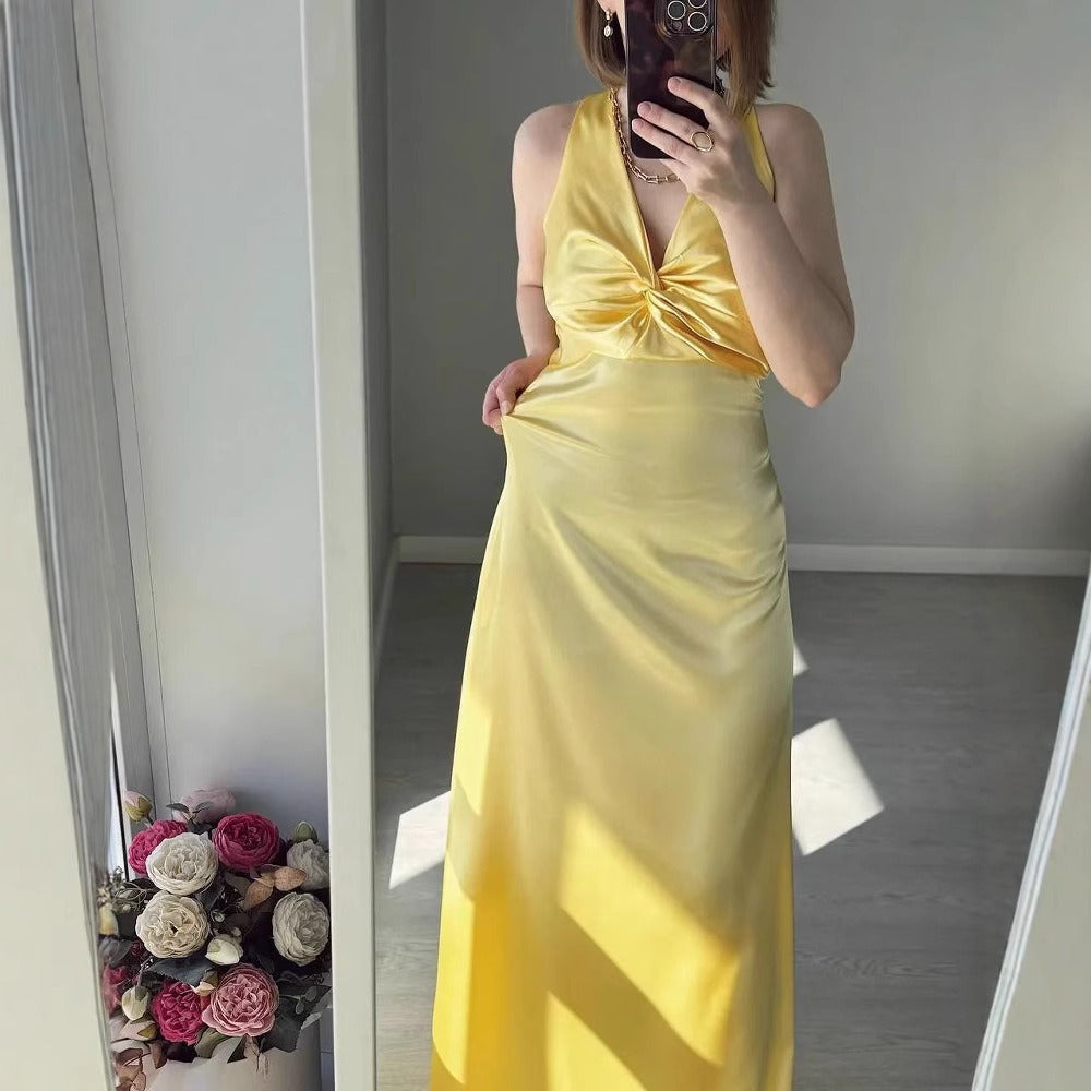 Woman in a yellow satin maxi dress with a twisted halter neckline, shown in a mirror