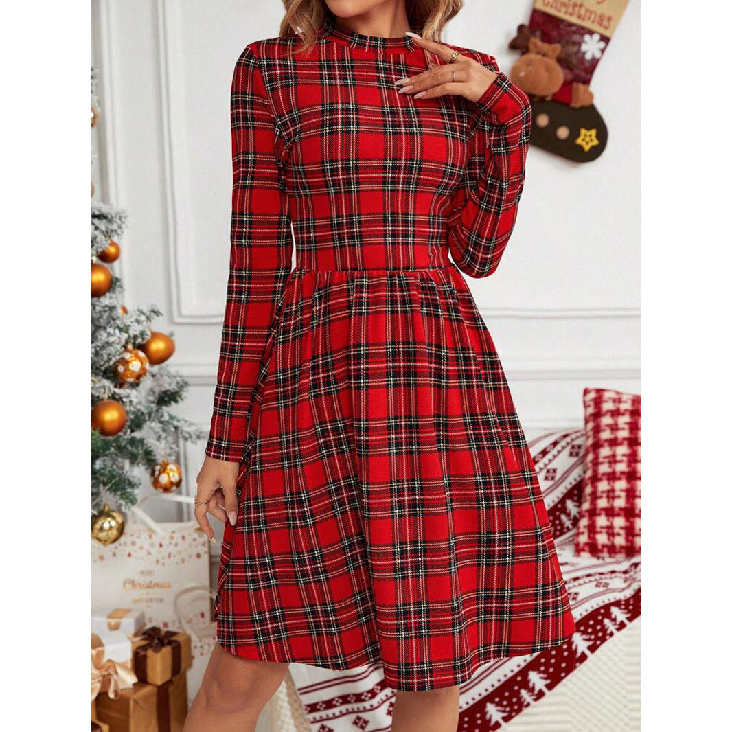 Close-up of a woman in a red plaid long-sleeve fit and flare dress with a round neck, posing in a festive setting.