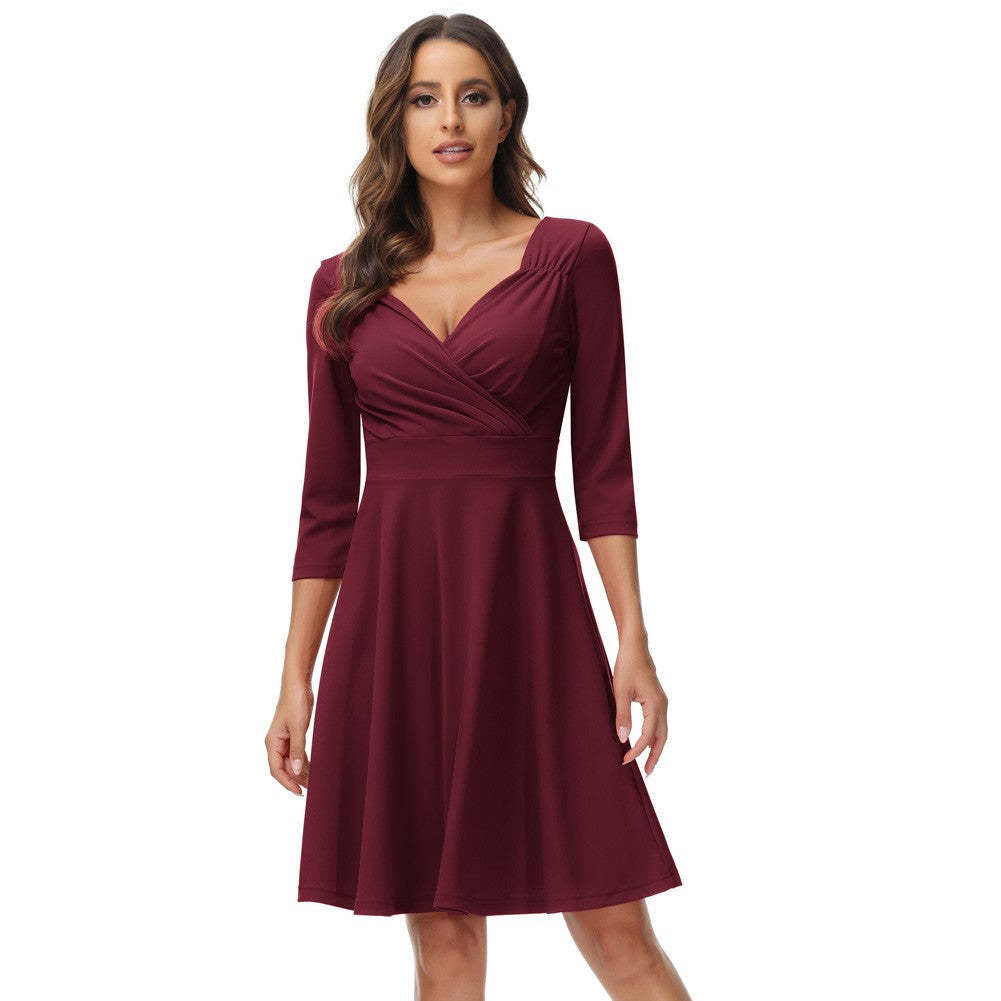 Woman wearing a burgundy fit and flare dress with a surplice neckline and three-quarter sleeves.