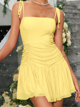 back view of a woman in a yellow ruched mini dress showing the open back and tie straps