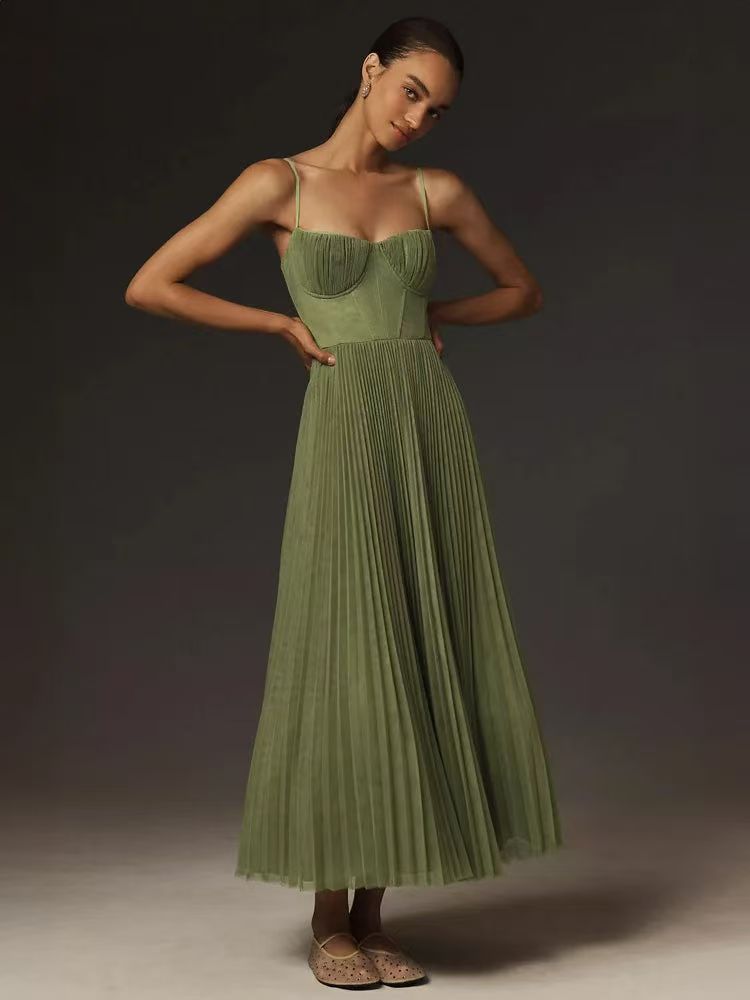 Woman wearing a green pleated midi dress with spaghetti straps and a sweetheart neckline, standing with hands on hips.