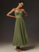 Woman wearing a green pleated midi dress with spaghetti straps and a sweetheart neckline, standing with hands on hips.