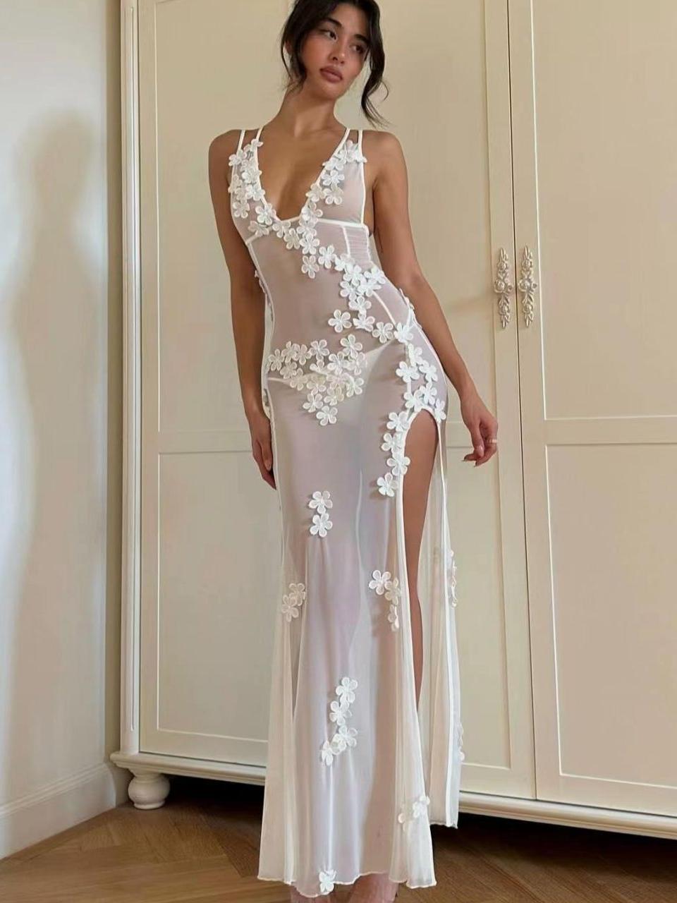 Woman wearing a long, sheer white dress with floral appliqués and a high slit.