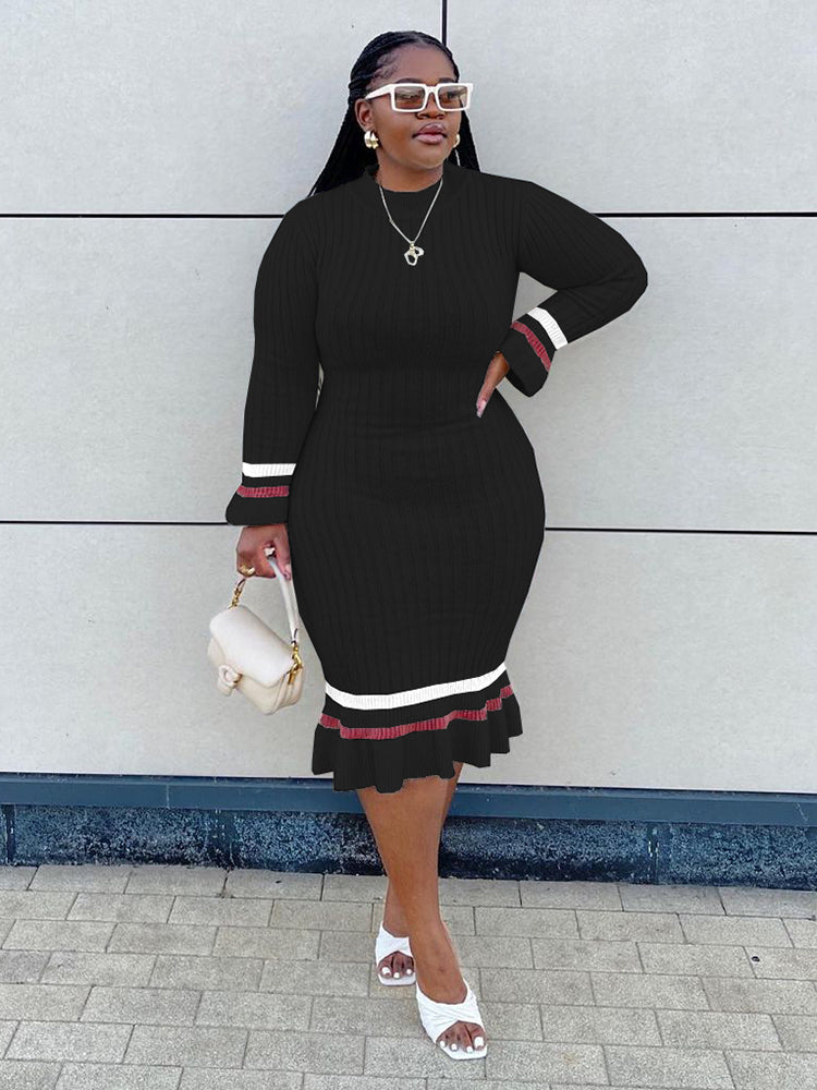 Woman wearing a black ribbed knit midi dress with striped cuffs and hem, holding a white handbag.