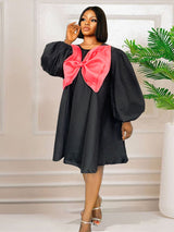 Woman wearing a black A-line dress with a large pink bow detail on the chest and voluminous sleeves.
