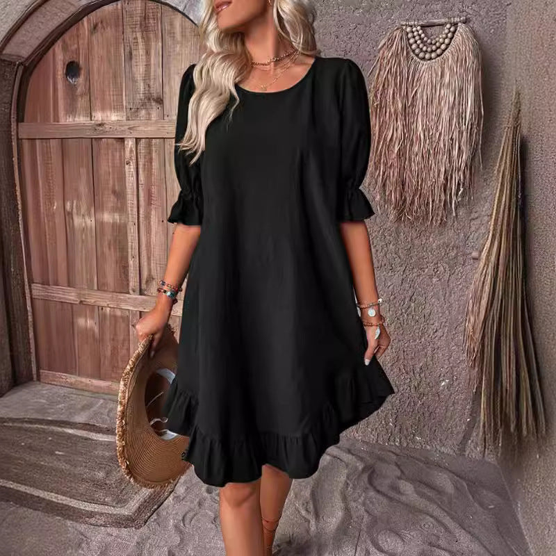 Woman wearing a black short puff sleeve A-line dress with a ruffled hem and neckline, holding a straw hat.