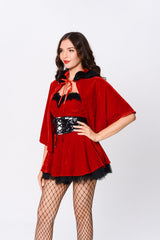 Woman wearing a red velvet costume with a cape, corset belt, and fishnet stockings, posing with one hand on her hip and looking to the side.