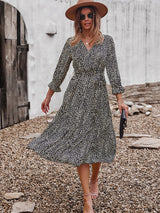 Woman twirling in a black and yellow polka dot midi dress, brown hat, and sunglasses.