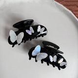 Two black claw hair clips with white iridescent butterfly embellishments and gem accents arranged on a light-colored surface.