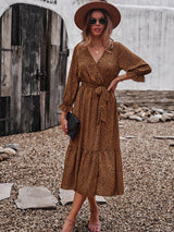 Woman wearing a brown and black polka dot midi dress, brown hat, sunglasses, and holding a black clutch.