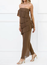 Side profile of a woman wearing a brown strapless tiered ruffle maxi dress with a sheer overlay.