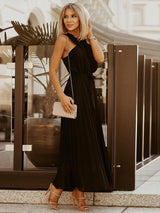Woman wearing a black pleated maxi dress with a halter neckline and a small clutch bag.