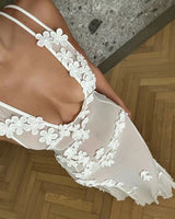 Close-up of a woman's chest and shoulder wearing a sheer white floral applique dress.