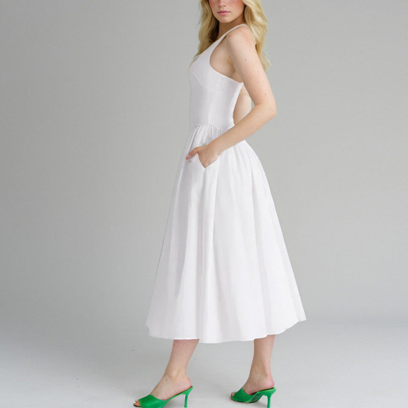 Woman wearing a white halter neck midi dress with a deep V-neckline and full skirt, with one hand in a pocket, against a gray background.