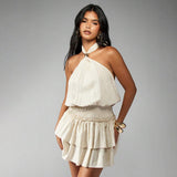 Front view of a woman modeling a cream tiered mini dress with a halter neckline.