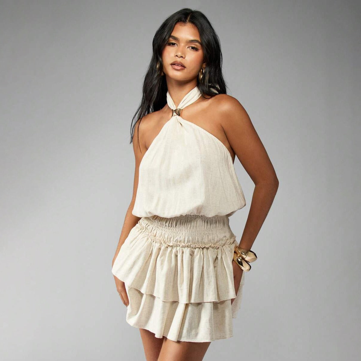 Front view of a woman modeling a cream tiered mini dress with a halter neckline.