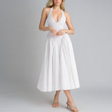 Full shot of a woman in a white halter neck dress with a deep V-neck and flowing skirt.