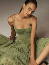 Woman wearing a green pleated midi dress with spaghetti straps and a sweetheart neckline, sitting on the floor with the dress draped around her.