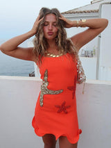 Woman in an orange sleeveless mini dress with starfish embellishments and a scalloped hemline, posing with hands on head.