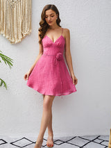 Woman wearing a pink mini dress with spaghetti straps and a v-neckline, standing and holding the hem of the dress.