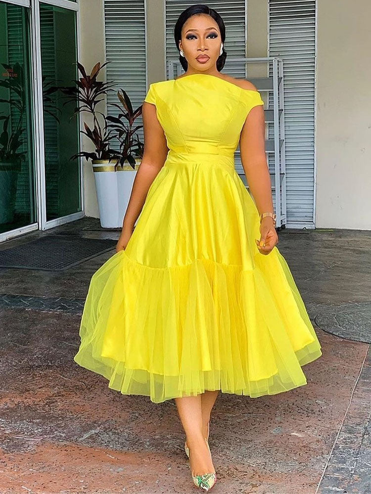 front view of a woman in a yellow satin dress with a flowing tulle overlay skirt