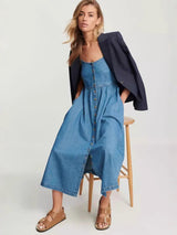 woman sitting on a stool wearing a blue denim midi dress and a blazer draped over her shoulders