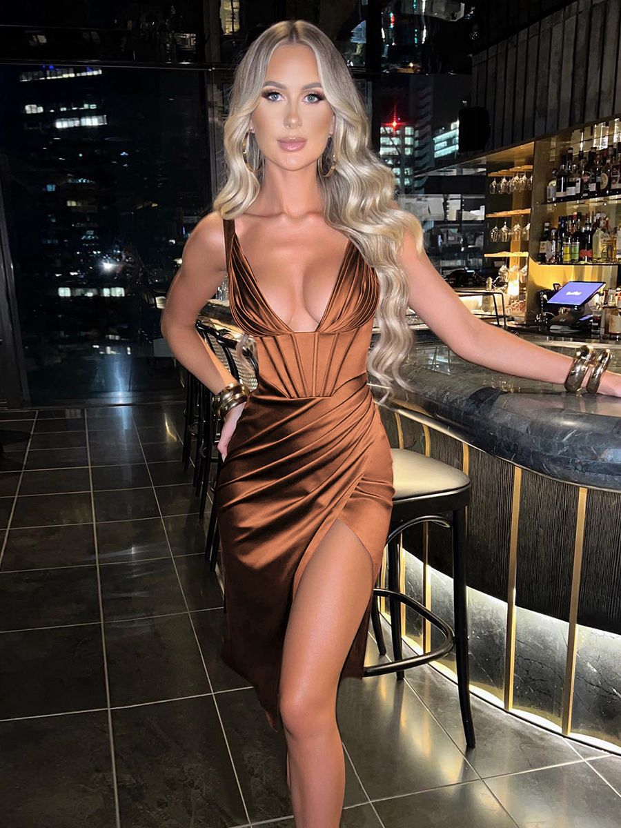 Woman in a brown satin dress with a plunging neckline and high slit standing at a bar.