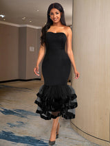 Woman wearing a black strapless mermaid dress with a tiered ruffled skirt and ribbon accents, standing in a hallway.