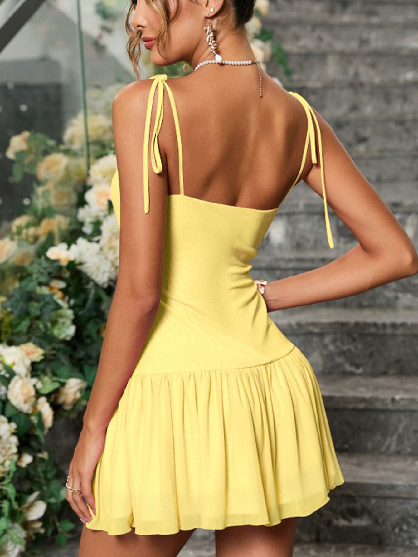 woman wearing a yellow ruched mini dress with tie shoulder straps and silver clutch