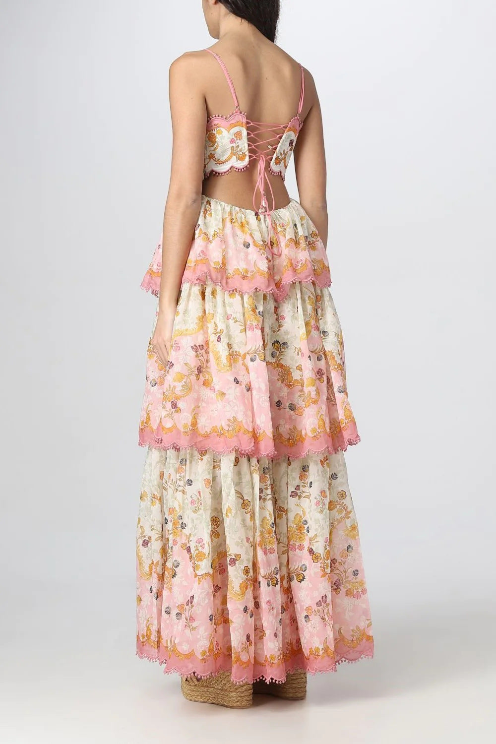 Back view of a woman wearing a tiered floral print maxi dress with a lace-up back and spaghetti straps.