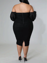 Back view of a woman in a black off-the-shoulder ruched midi dress with sheer puff sleeves.
