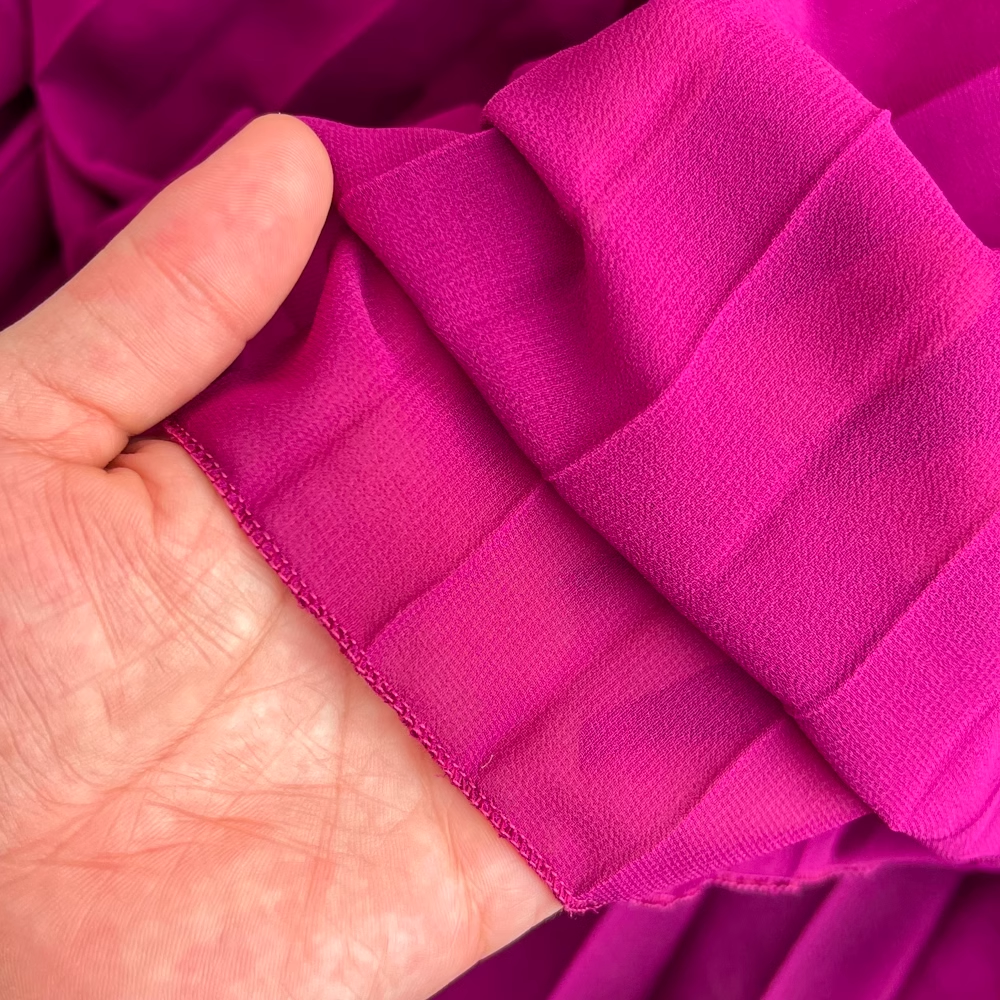Hand holding a swatch of magenta chiffon fabric with fine pleats.