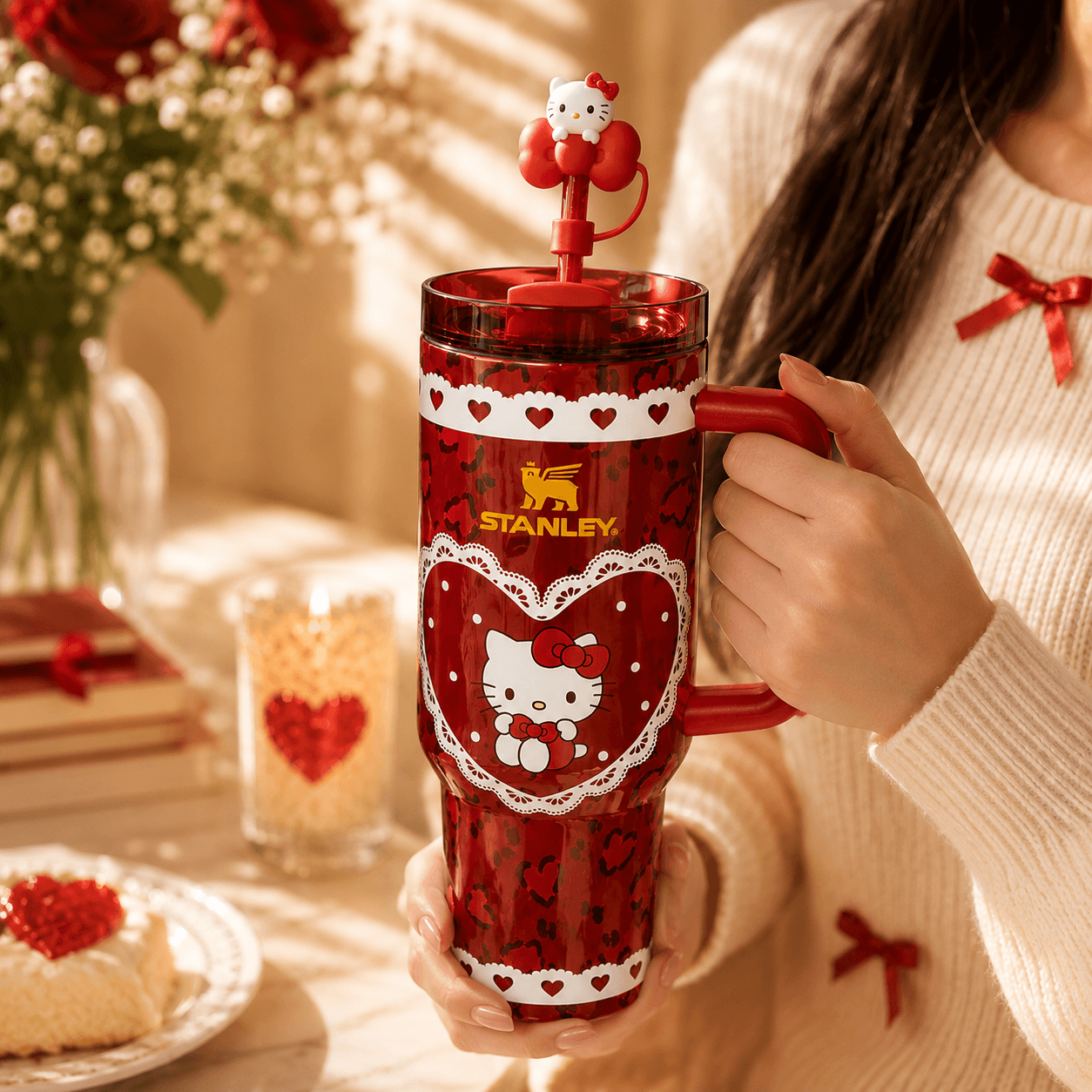 Person holding a red Stanley tumbler with Hello Kitty design, surrounded by festive decor.