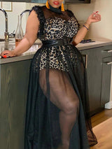Woman wearing a leopard print top with a sheer black mesh overlay maxi skirt and a wide black belt, leaning against a kitchen counter.